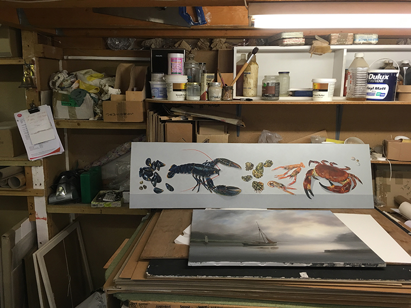 The Coombe Gallery framing workshop above Foss Street, paint tins, brushes, a long seafood watercolour on the bench and a moody seascape leaning below.